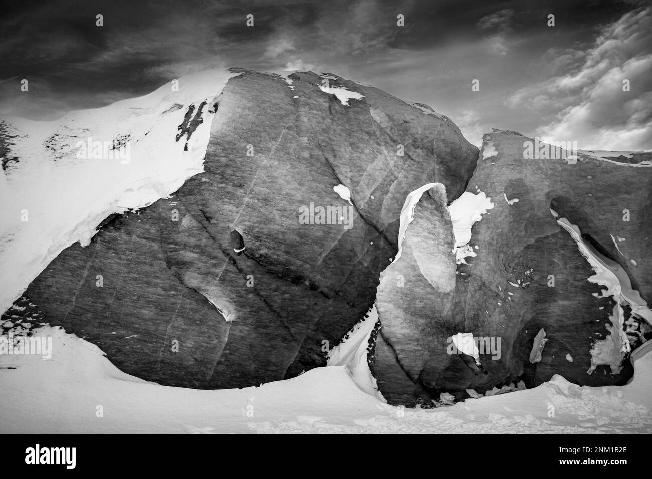 A high contrast black and white shot of a large rock formation on a snow-covered mountain peak Stock Photo