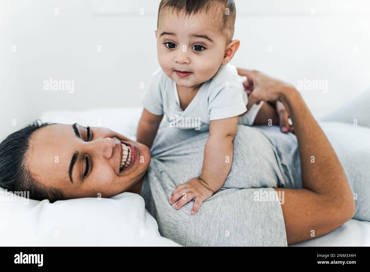 Happy joyful mother lying on bed with her small baby Concept family