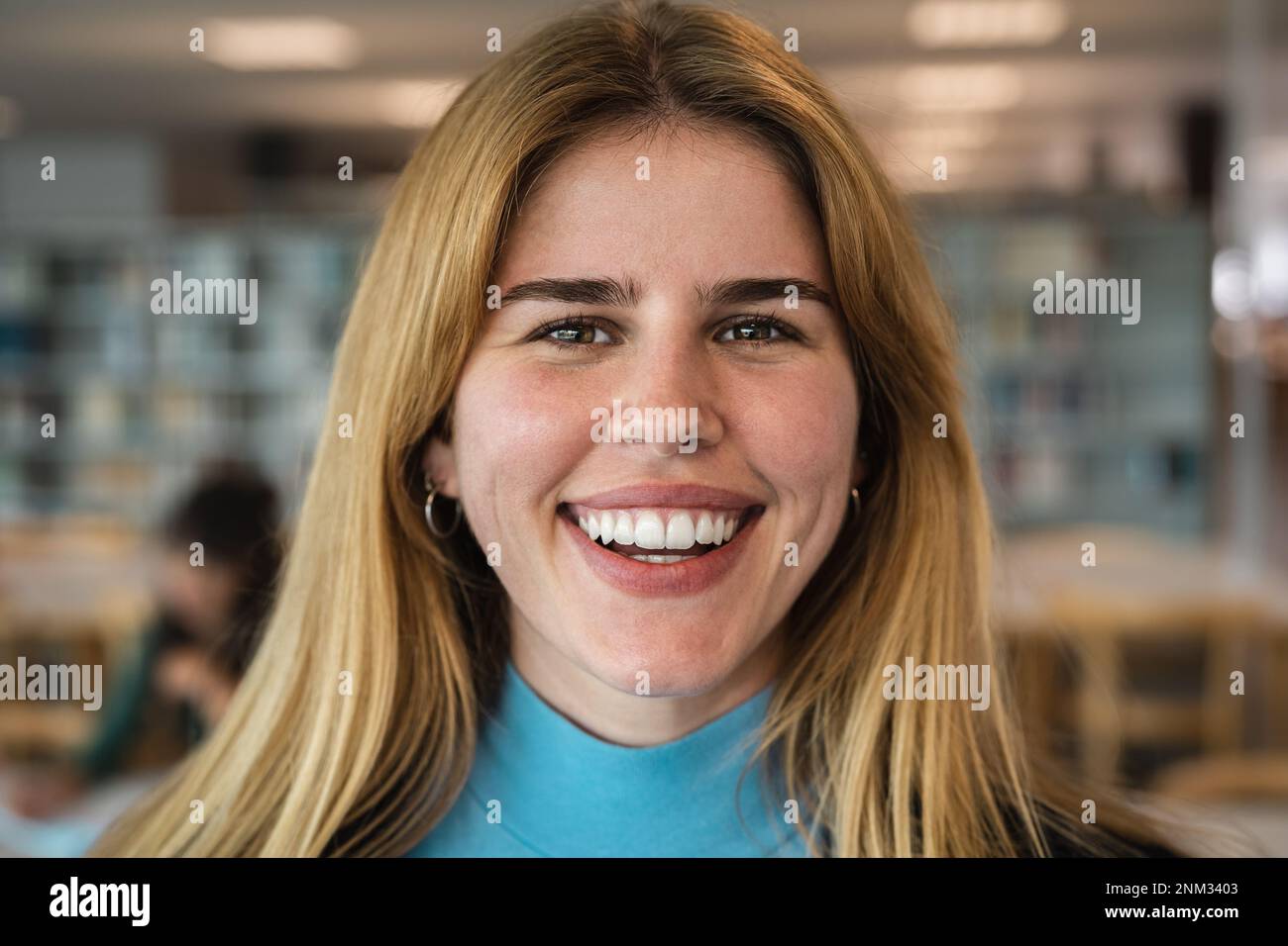 Happy young girl smiling into the camera while standing inside university library Stock Photo