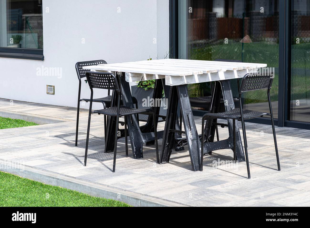 Terrace table made of white pallet standing on plastic trestles, black plastic chairs. Stock Photo