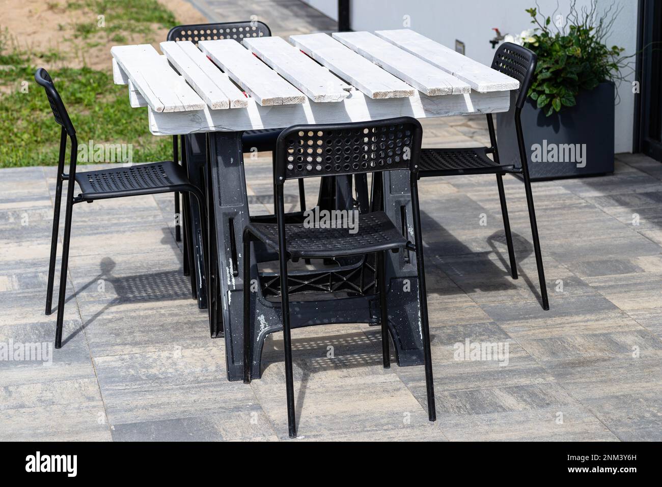 Terrace table made of white pallet standing on plastic trestles, black plastic chairs. Stock Photo