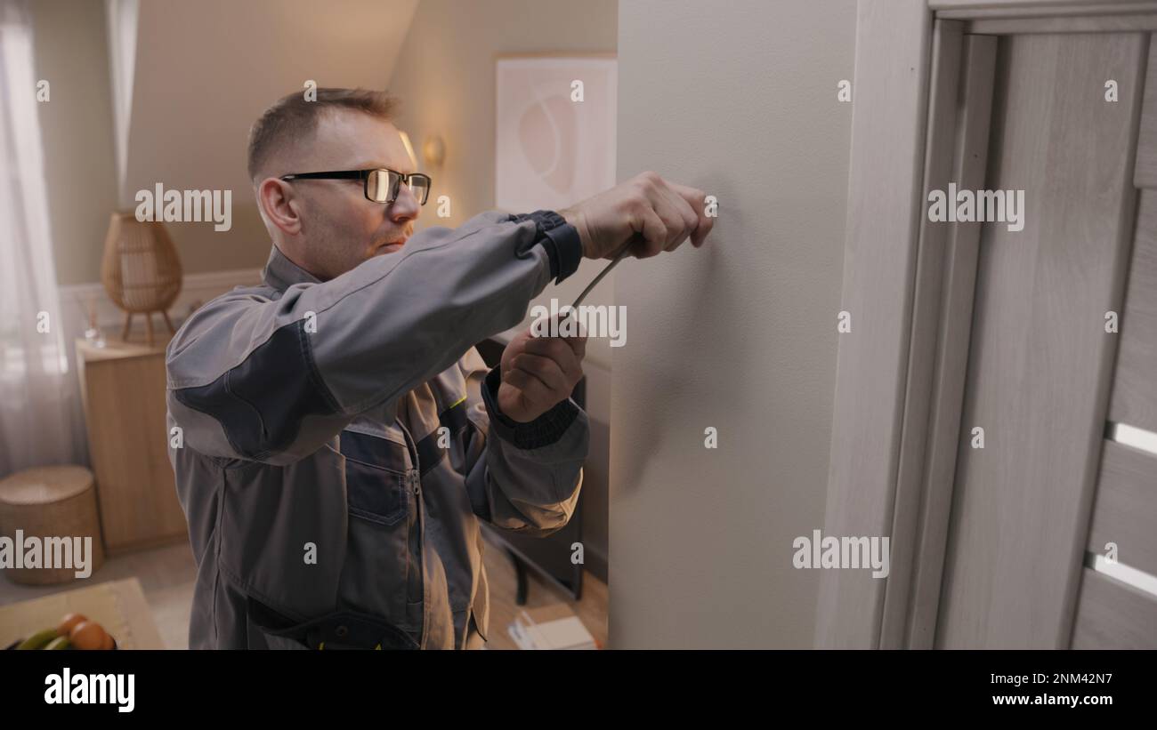 Man in uniform puts cable in drilled hole. Electrician removes