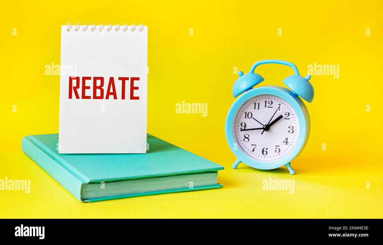 The word REBATE on a notebook and a yellow background, next to a clock and a diary Stock Photo