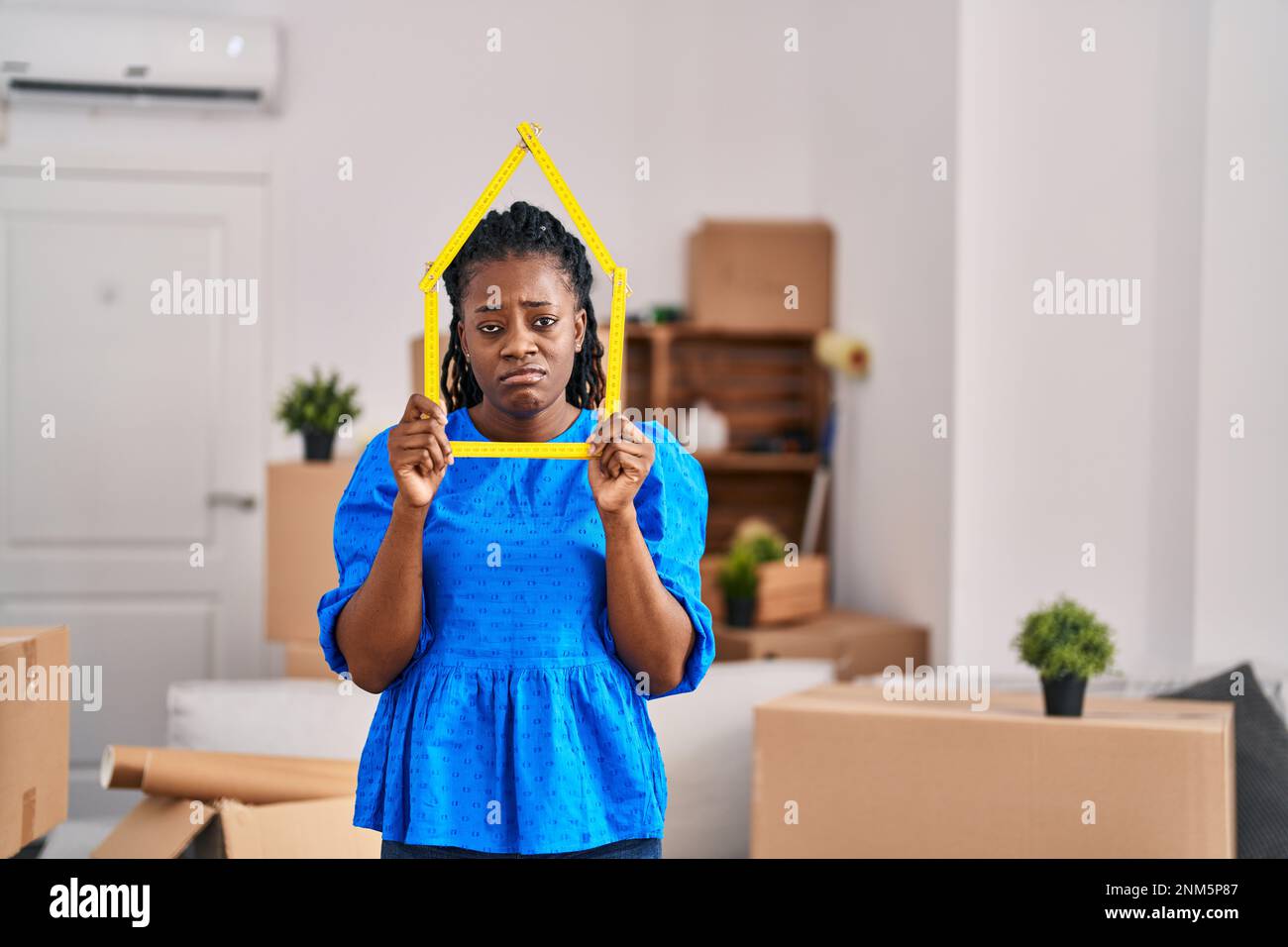 African woman with braided hair at new home holding ruler depressed and ...