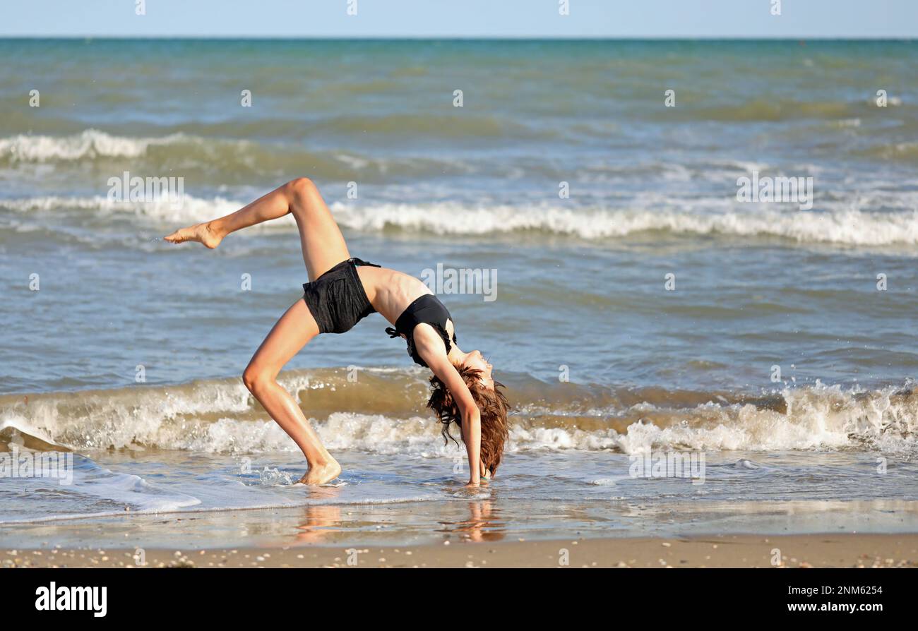 young barefoot girl in black swimsuit from rhythmic gymnastics exercises on the seashore Stock Photo