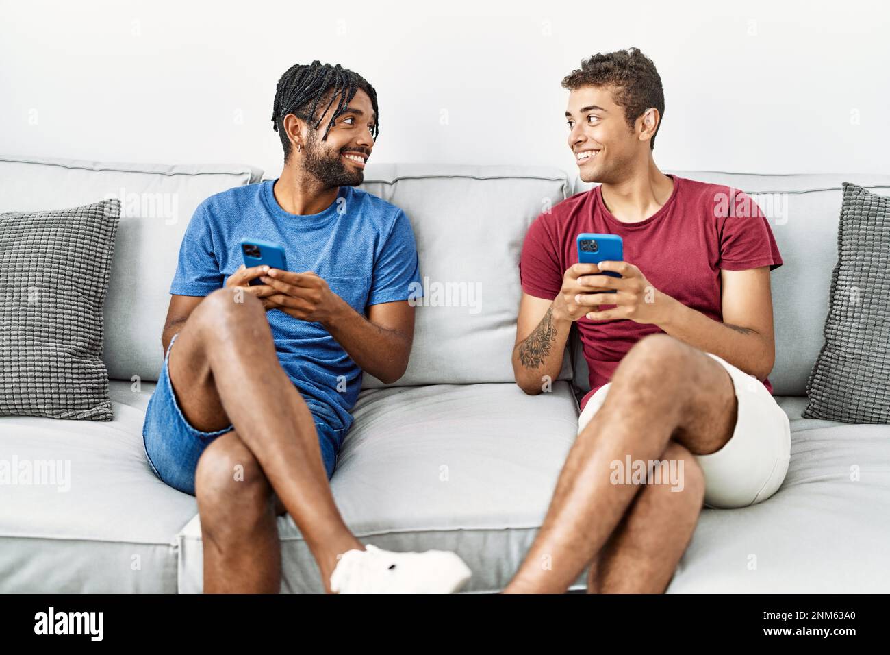 Two men friends using smartphone sitting on sofa at home Stock Photo