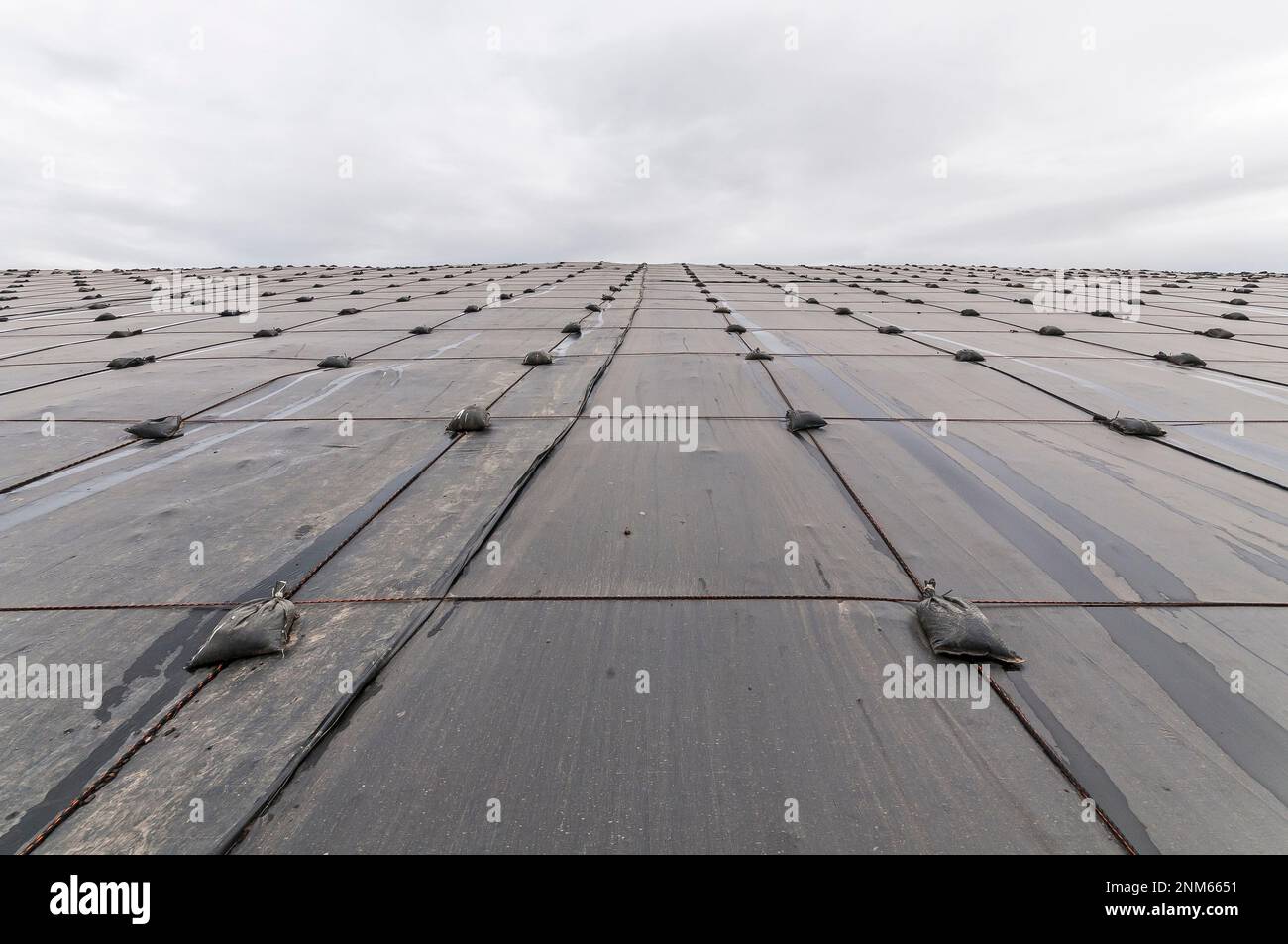 Weighted plastic sheeting covers a hillside in an active landfill.  Probably PVC geomembranes. Stock Photo