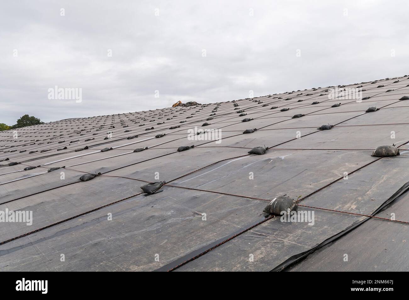 Weighted plastic sheeting covers a hillside in an active landfill.  Probably PVC geomembranes. Stock Photo