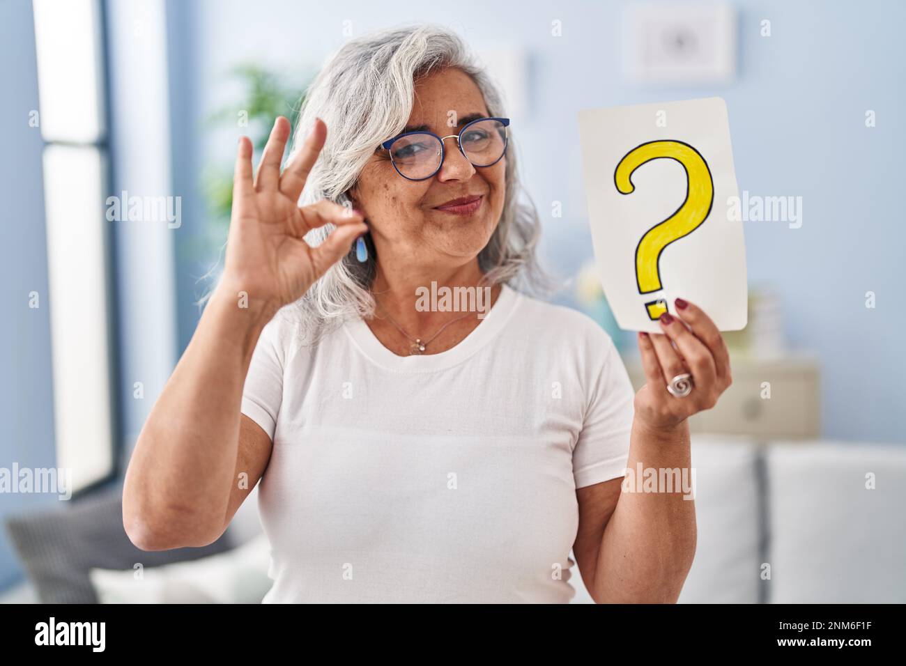 Middle age woman with grey hair holding question mark doing ok sign ...