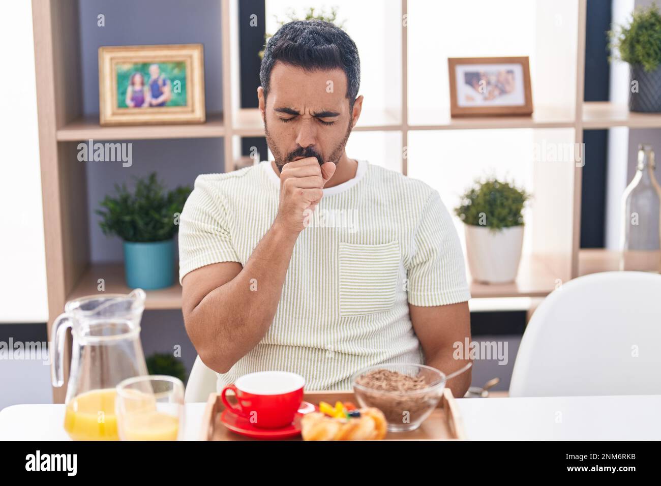 Hispanic man with beard eating breakfast feeling unwell and coughing as symptom for cold or