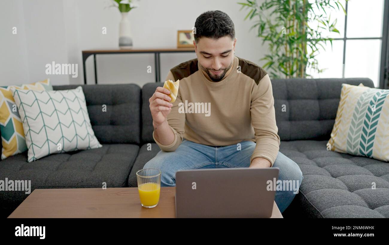 Young arab man having breakfast using laptop at home Stock Photo