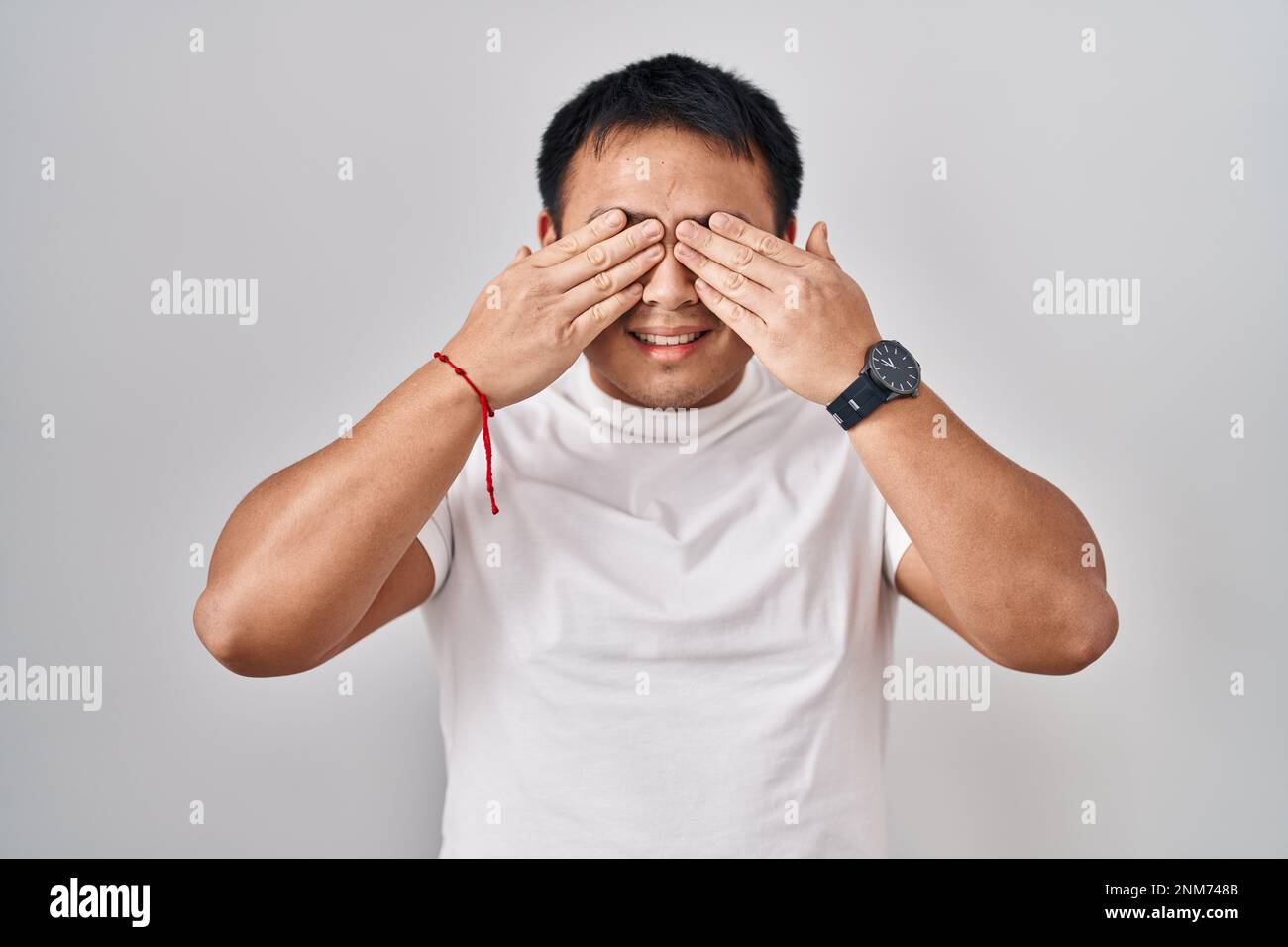 Young chinese man standing over white background covering eyes with hands smiling cheerful and funny. blind concept. Stock Photo