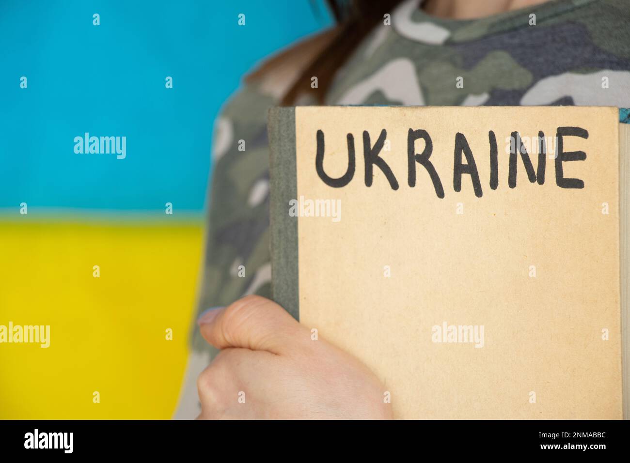 A girl in camouflage with a book on which Ukraine is written against the background of the flag of Ukraine, education in Ukraine during the war Stock Photo