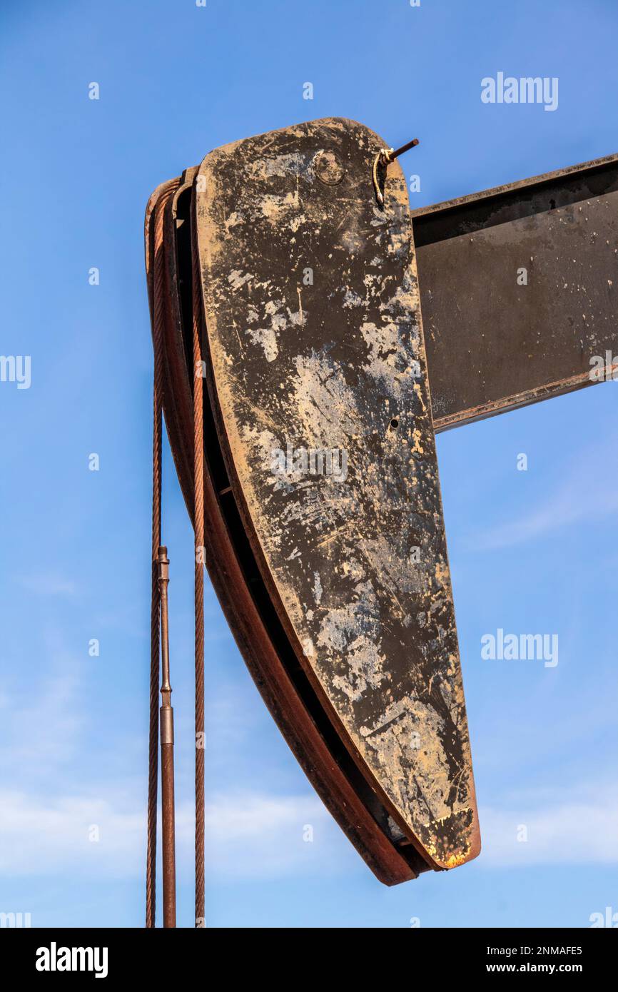 Closeup of rusty grungy horse head of an oil well with bridle or wireline  - cables- against blue sky Stock Photo