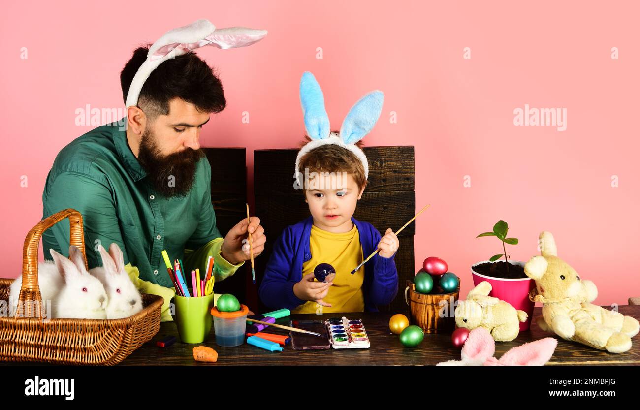 Easter family in bunny ears painting Easter eggs. Cute little child boy in rabbit ears on Easter day. Happy family father and son painting eggs for Stock Photo