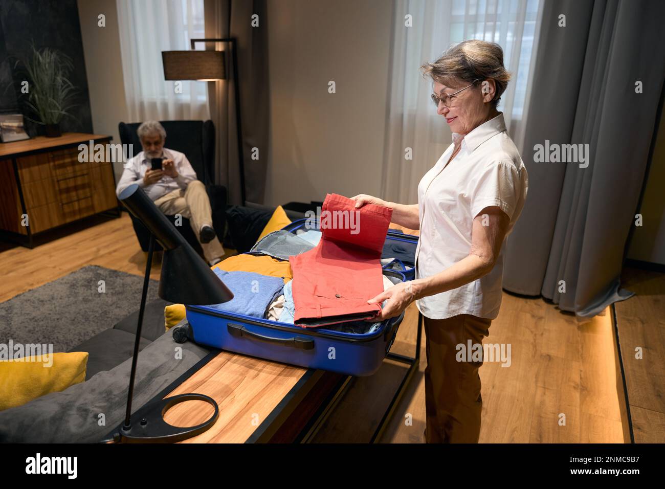 Old woman helping husband fold clothes in trolley bag Stock Photo Alamy