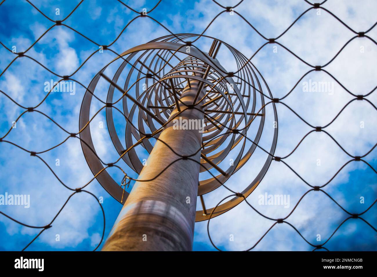Wind Spinner  mounted on playground climbing nets - seen through the mesh with focus on metal - distance Stock Photo