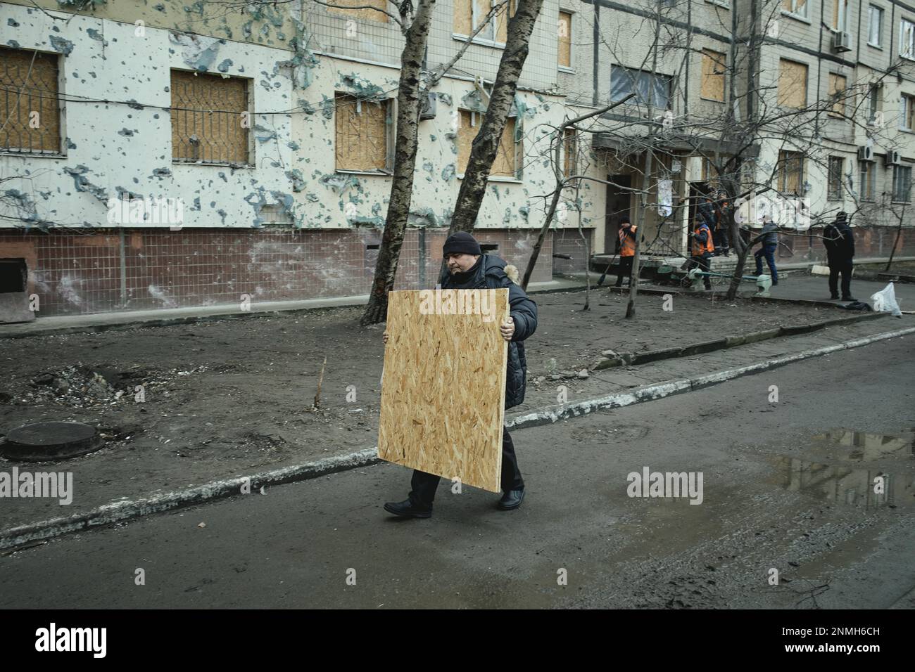 A man brings a chipboard to seal the destroyed windows of his flat after Russian missile attack on an apartment building on Jan. 14, 2023 also Stock Photo