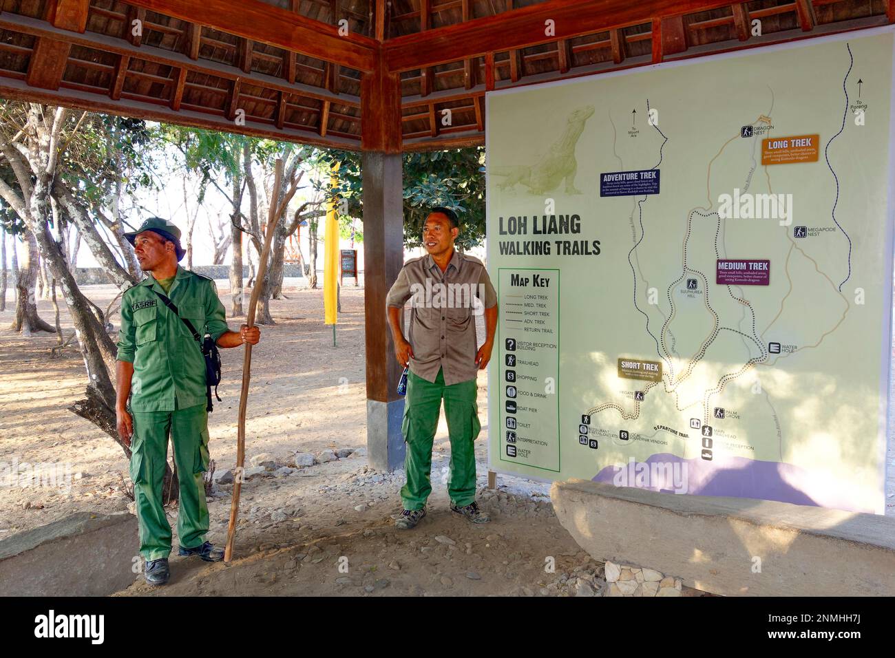 Park rangers, Indonesians, two, await visitors in reception in front of map with hiking trails, Komodo National Park, Unesco World Heritage Site Stock Photo
