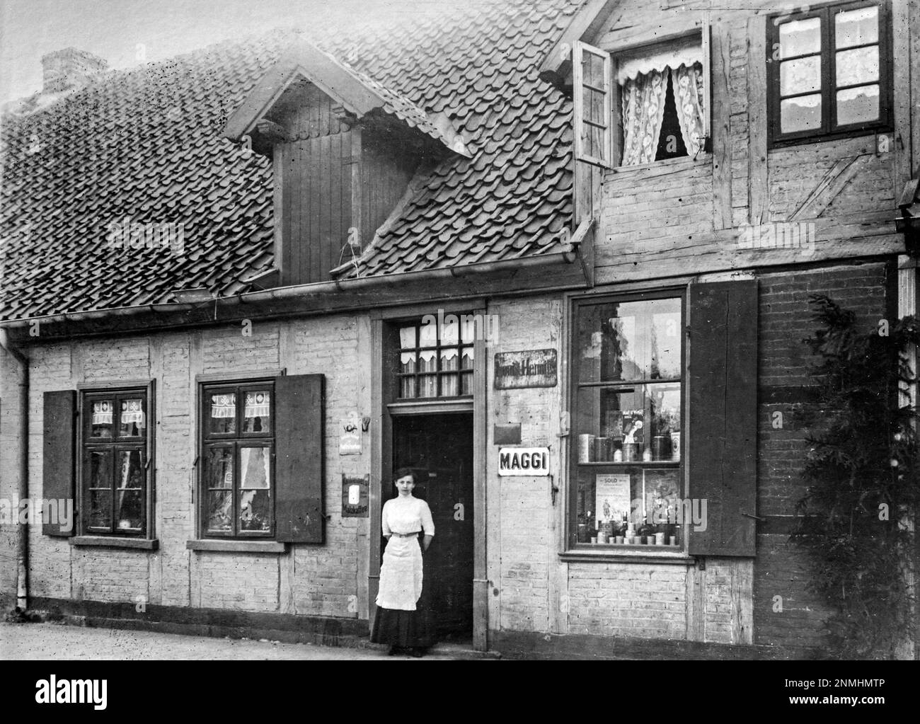 Young woman standing in the entrance, grocery shop, Lower Saxony, Germany, ca. 1920 Stock Photo