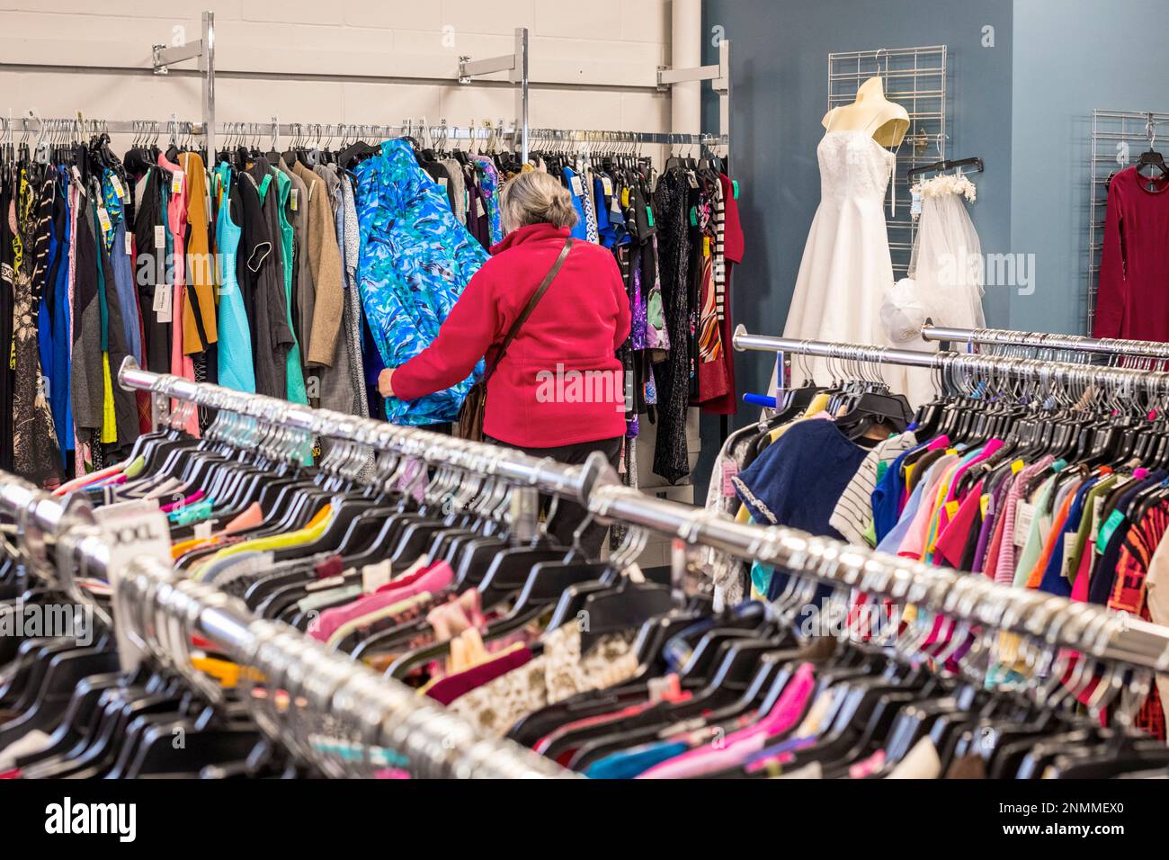 Senior woman in red jacket perusing through the used clothing racks at a thrift shore(Good Will) in Ludington, MI, USA. Stock Photo