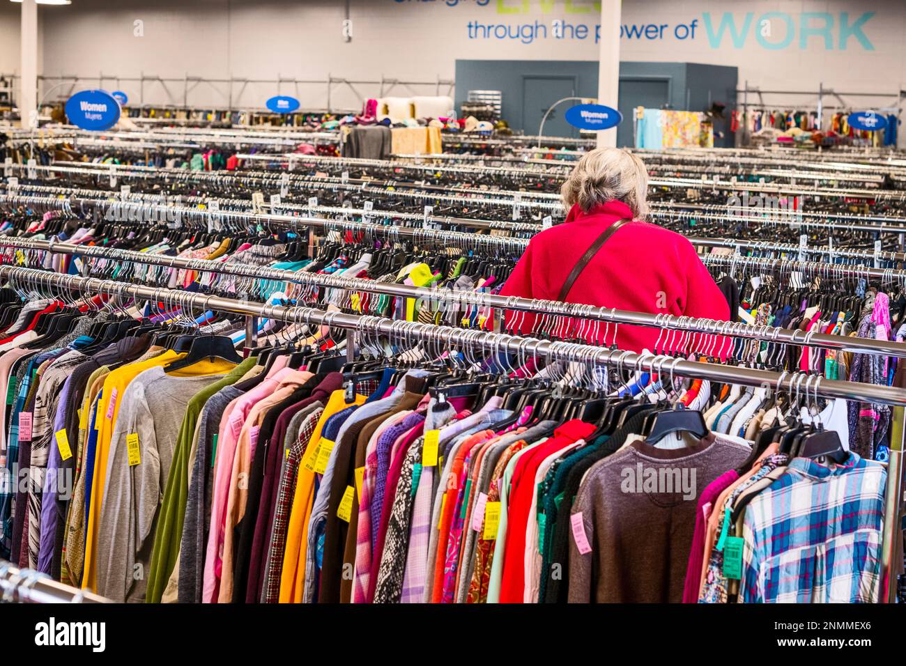 Senior woman in red jacket perusing through the used clothing racks at a thrift shore(Good Will) in Ludington, MI, USA. Stock Photo