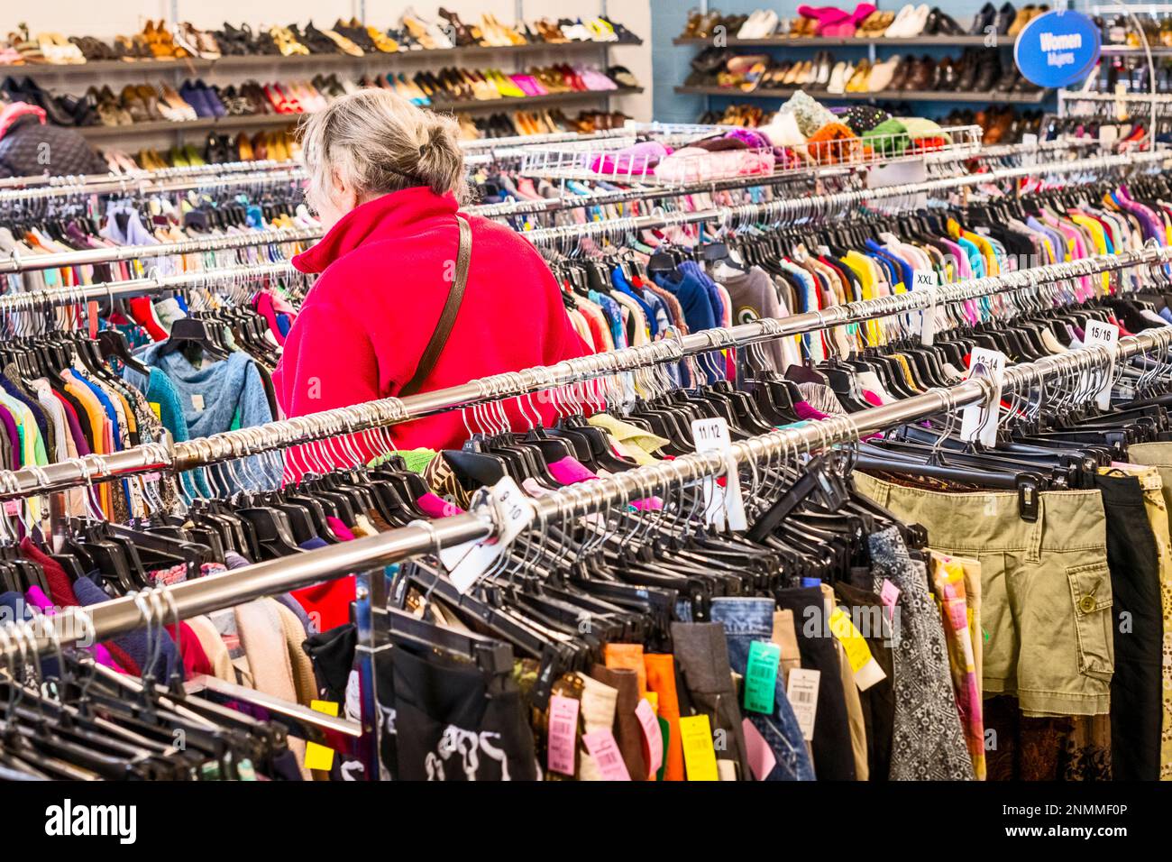 Senior woman in red jacket perusing through the used clothing racks at a thrift shore(Good Will) in Ludington, MI, USA. Stock Photo