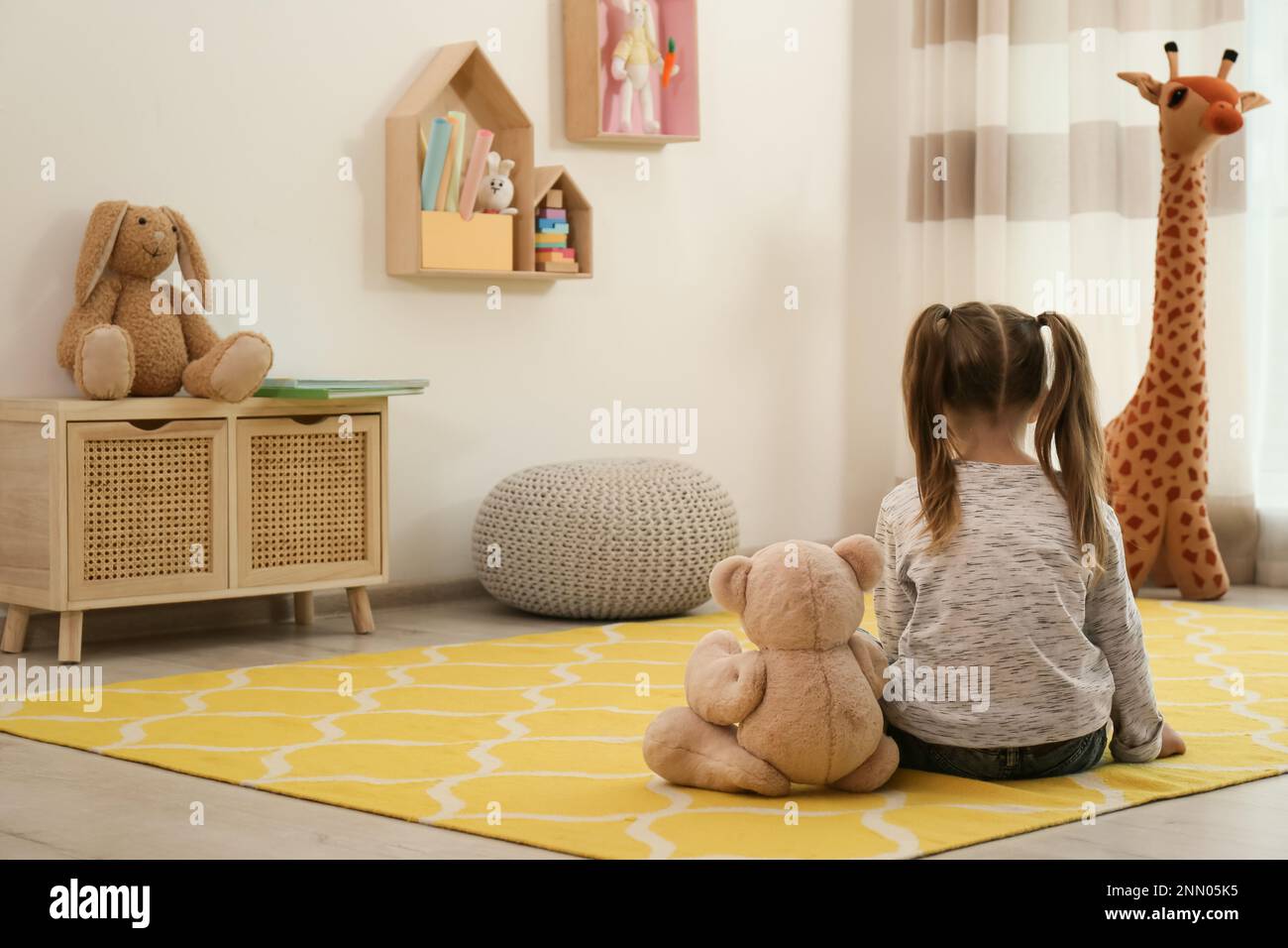 Lonely little girl with teddy bear sitting on floor at home, back view ...