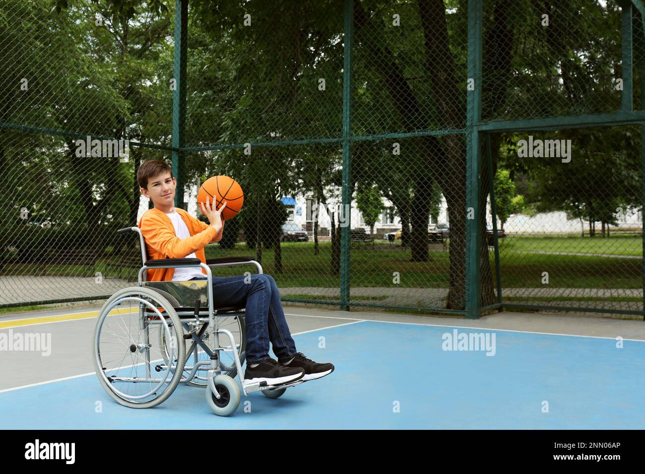 Disabled teenage boy in wheelchair playing basketball  on outdoor court Stock Photo