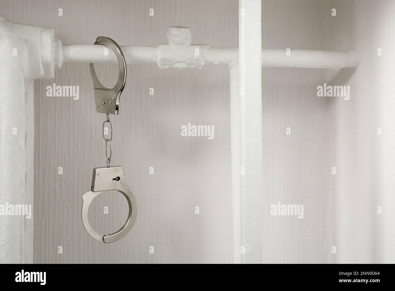 Handcuffs hanging on radiator near white wall indoors Stock Photo