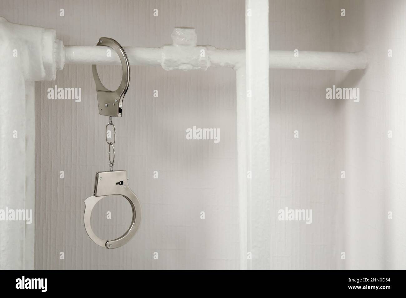 Handcuffs hanging on radiator near white wall indoors Stock Photo - Alamy