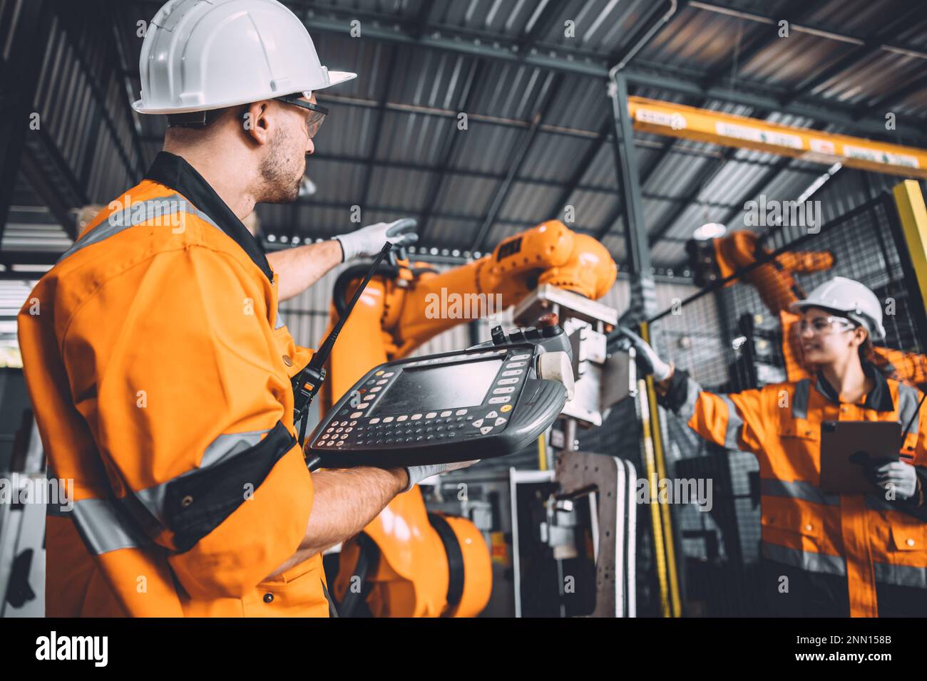 Engineer team service robot welding working in automation factory. People worker in safety suit work robotic arm software programming or replacing par Stock Photo