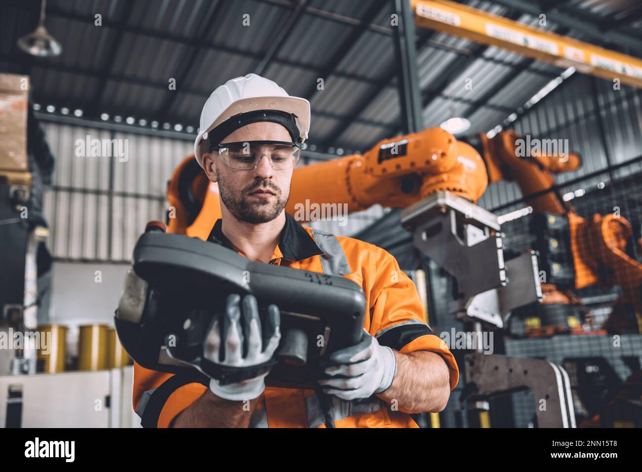 Engineer team service robot welding working in automation factory. Male worker operate robotic arm software hand controller in automated manufacturing Stock Photo