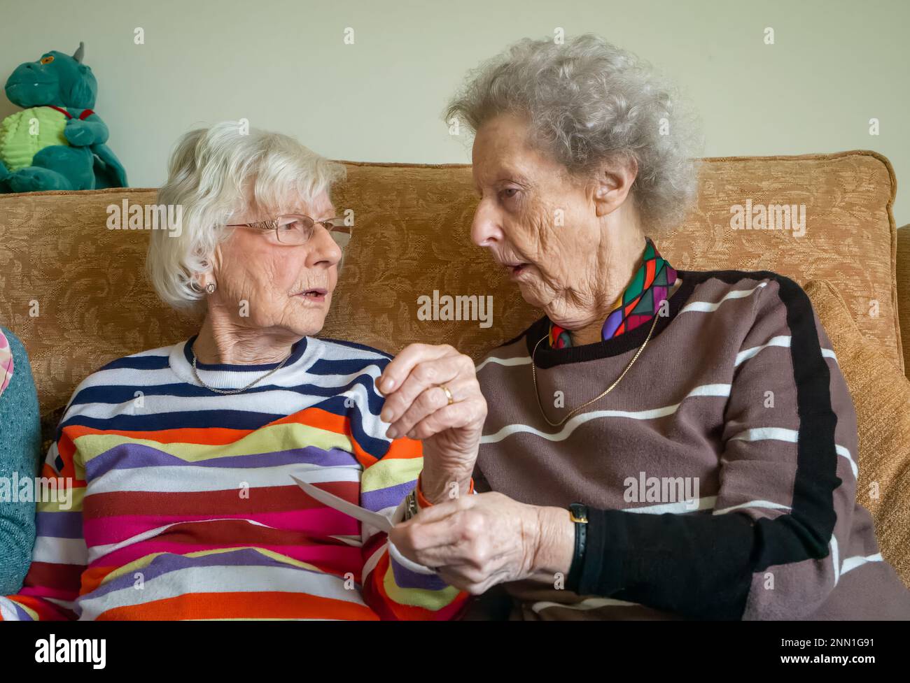 Two elderly women in their 90s who are lifelong friends sit, look at a photograph and chat about the old days. Stock Photo