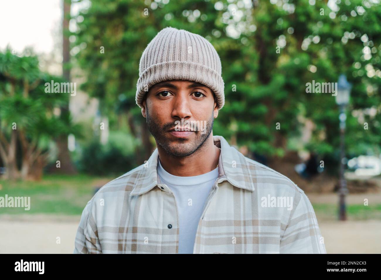 Close up portrait of young attractive african american man with beanie hat looking serious at camera. Front view of a hispanic guy standing in a park outdoors with sad attitude. High quality photo Stock Photo