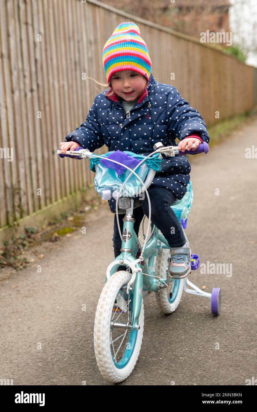 Child learning to ride a bicycle with stabilisers Stock Photo