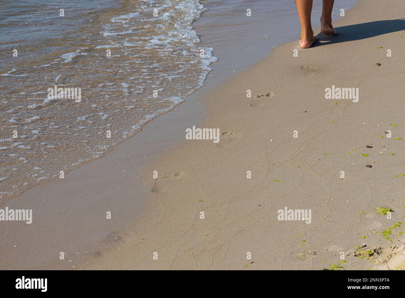 Footprints of a man on the yellow beach sand from walking barefoot by the sea with water that washes away the footprints. Contemplation of life Stock Photo