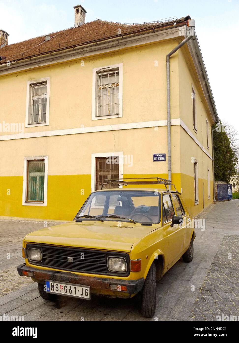 A yellow Zastava 101 parked infront of a yellow-painted house in Novi Sad, Serbia Stock Photo