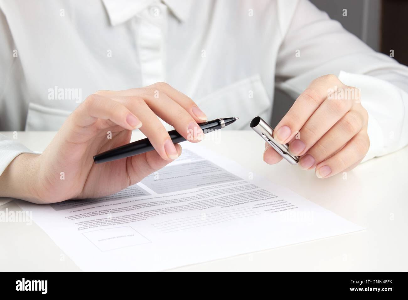 A young woman in a white blouse - A Young Woman In A White Blouse Removes The Cap From A Pen To Start Filling Out Bills Resumes Documents 2NN4FFK 