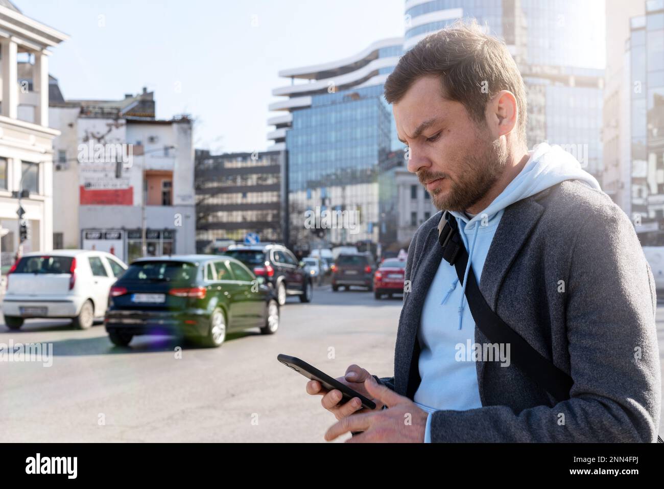 Around Mobile Man standing near the road in city and looking at screen of his ...