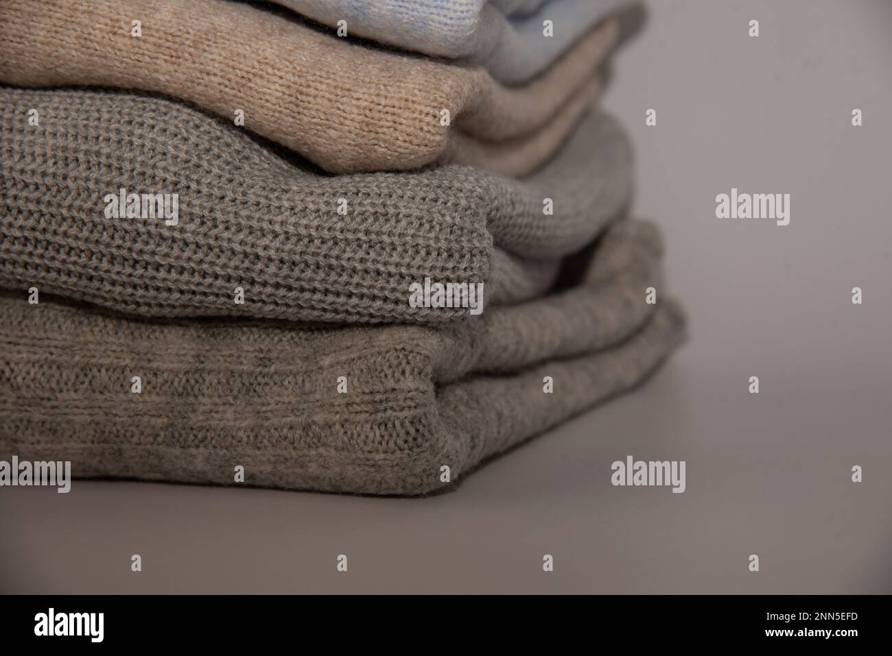 knitted warm pastel color sweaters with different knitting patterns folded in stack, Close up, copy space for text. Stock Photo