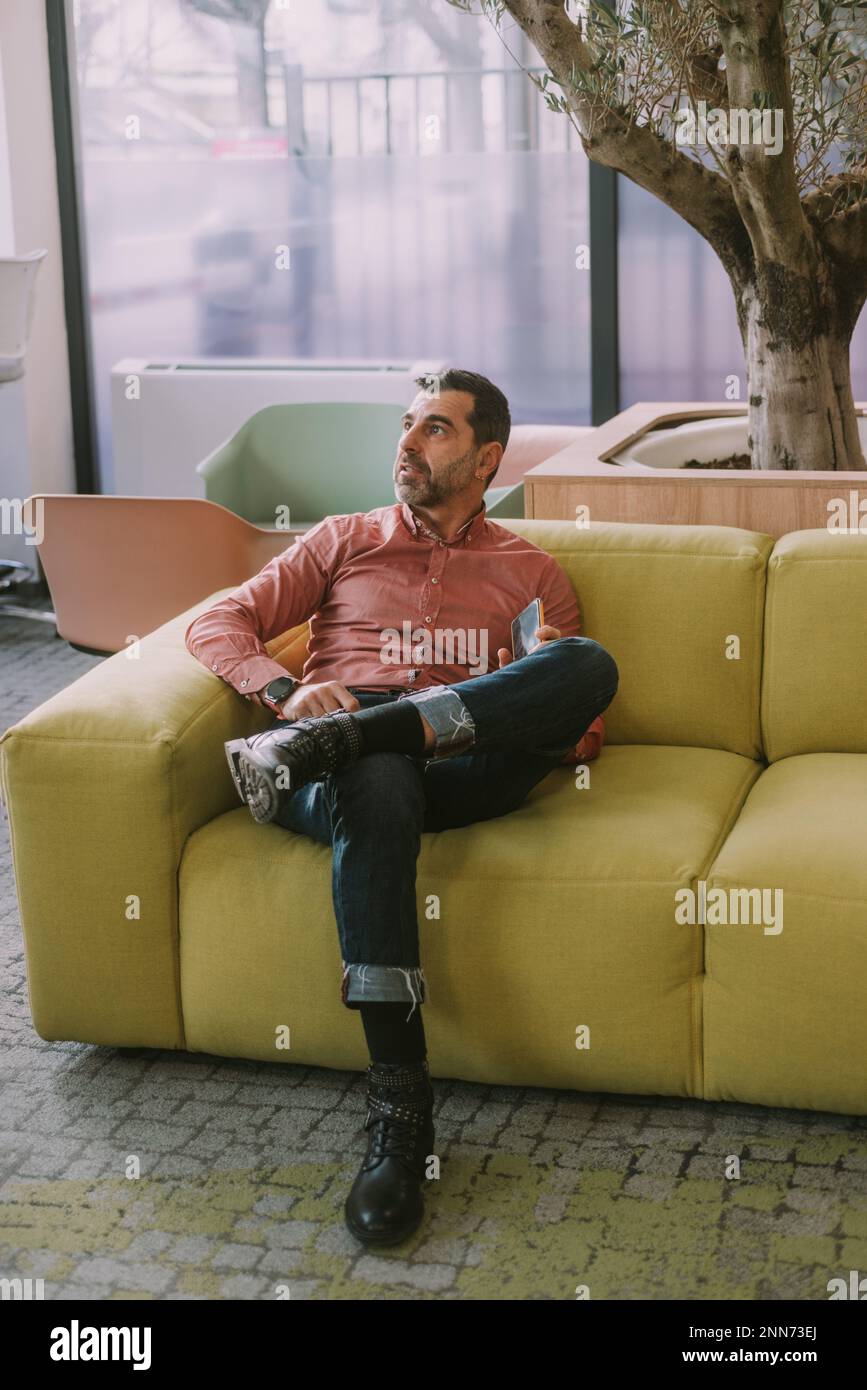 Handsome older business man looking up while sitting on the yellow couch at the co working space Stock Photo