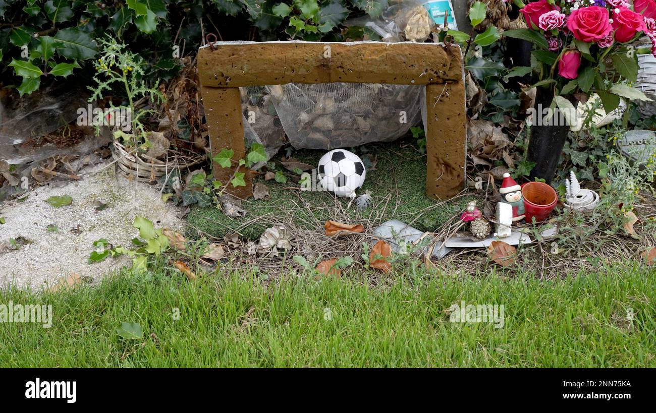 A more recent sight are the small mini-shrines which seem to be appearing as relatives attempt to come to terms with the death of younger relatives in particular.  The tiny football goal made of flower arranger's foam is one, complete with a net made from curtaining and a sad little collection of bits of old plastic with just the penguin in a hat and scarf still recognisable. More miscellaneous bric a brac surrounds the grey pot holder at the other shrine.  The concrete owl is easily explained as a symbol of a local Sheffield football team. The fading print on a tin of Carling suggests decay Stock Photo