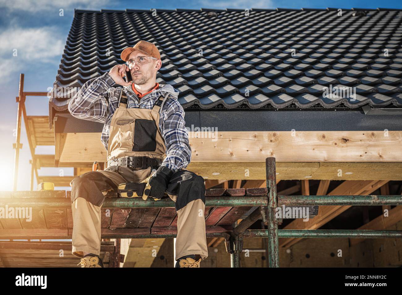 Caucasian Contractor Talking on the Phone While Sitting on Scaffolding ...