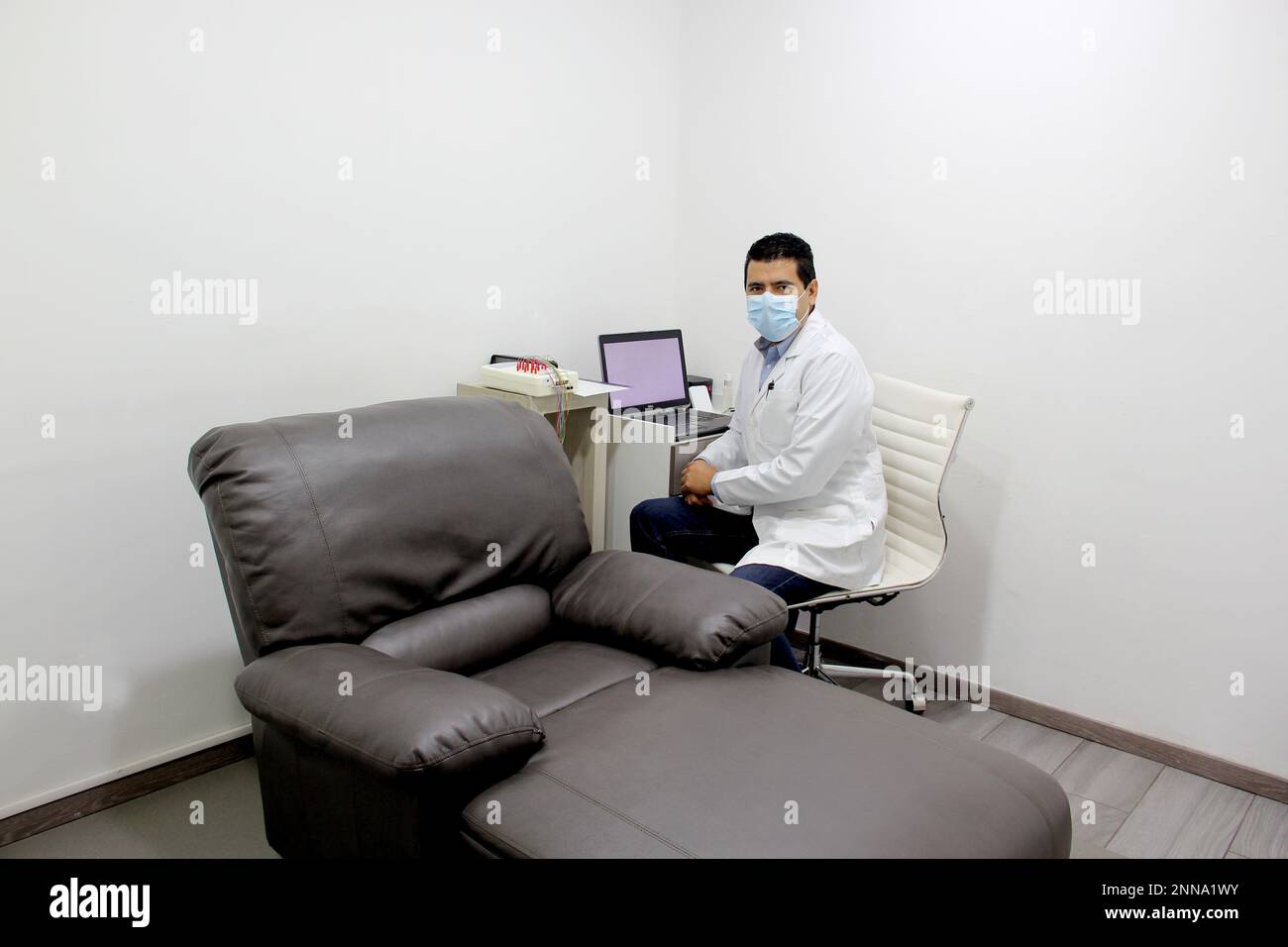 Latin doctor neurologist specialist doing electromyography nerve and muscle study in white office with armchair Stock Photo