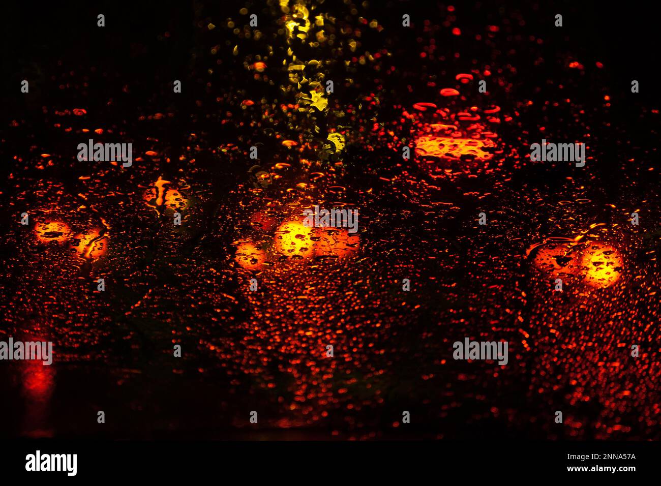 Rain drops on glass surface with red bokeh night city lights from a ...