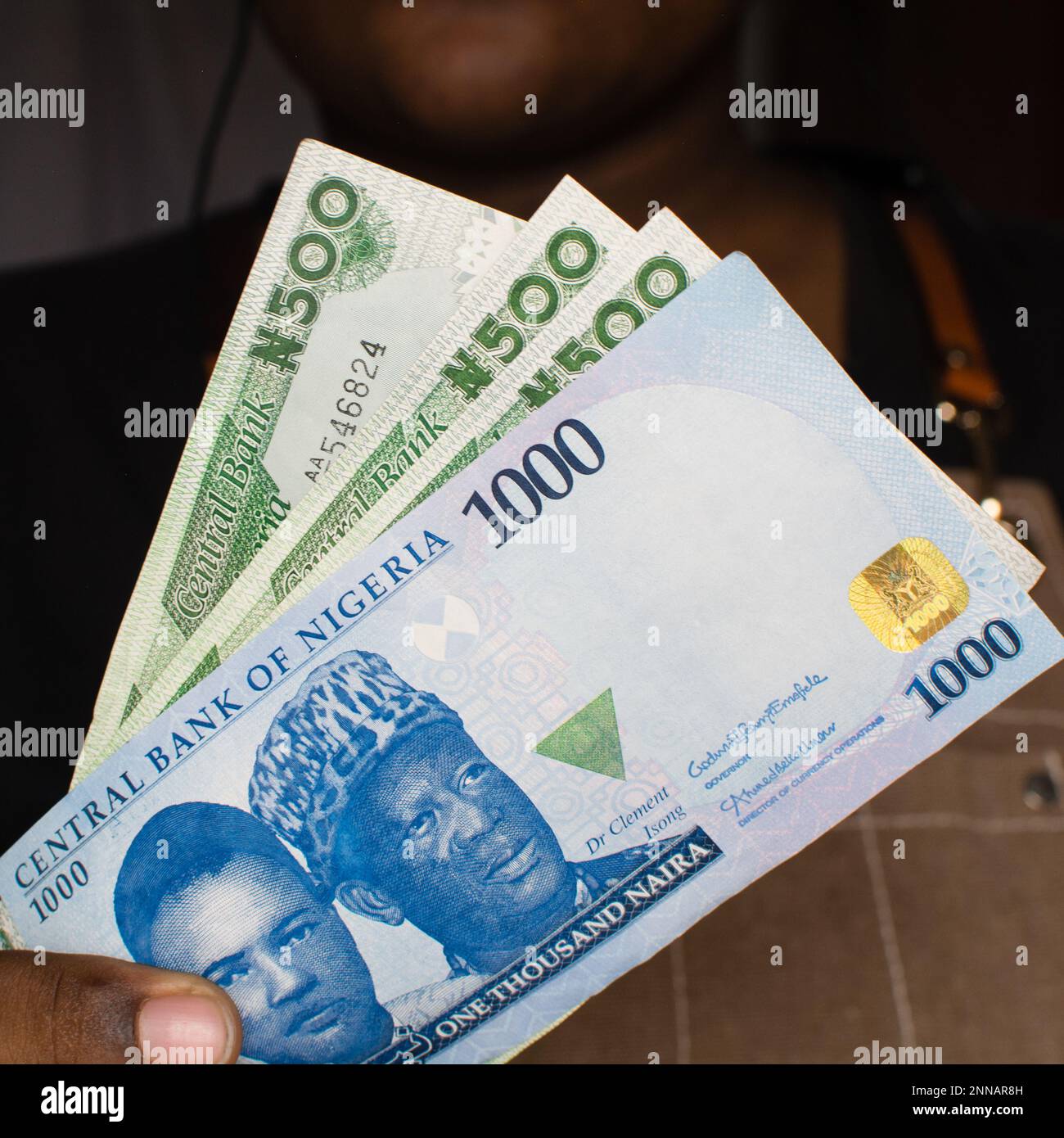 Hand holding the new Nigerian 1000 and 500 Naira notes on a white