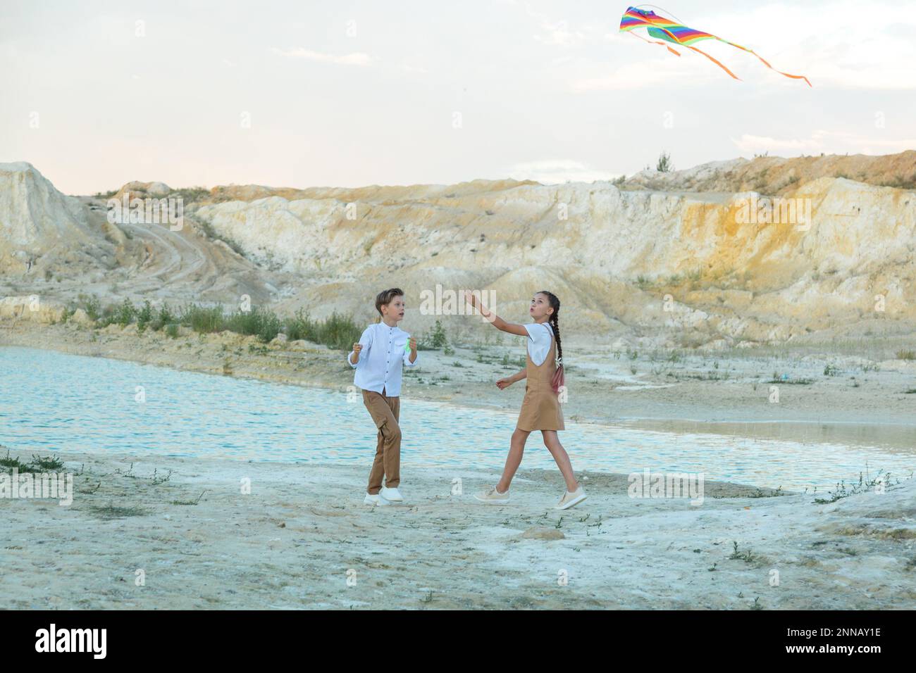 A boy and a girl launch bright kite standing on the edge of a mountain near pond. Stock Photo