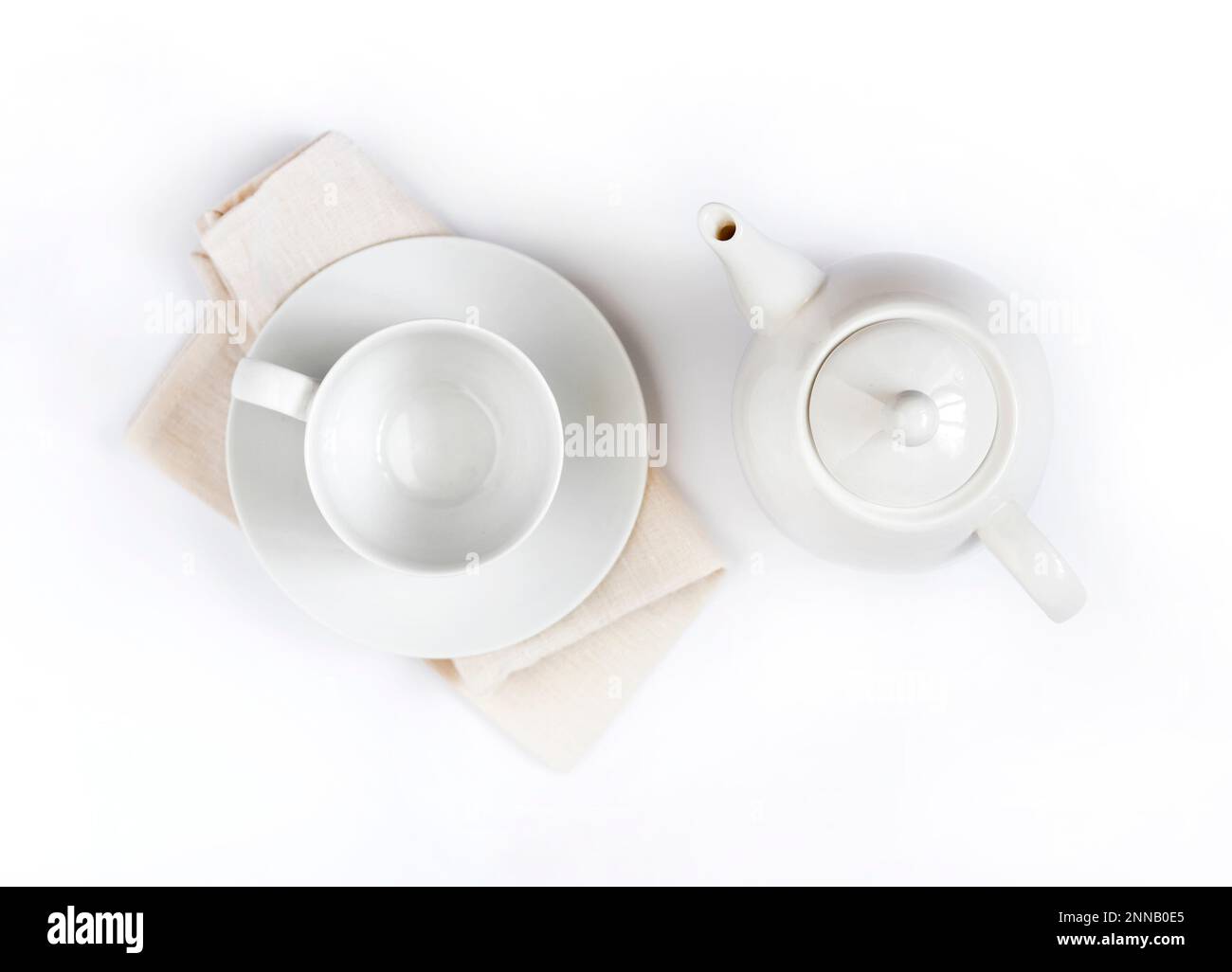 White teapot and empty teacup on pale beige cloth isolated on white
