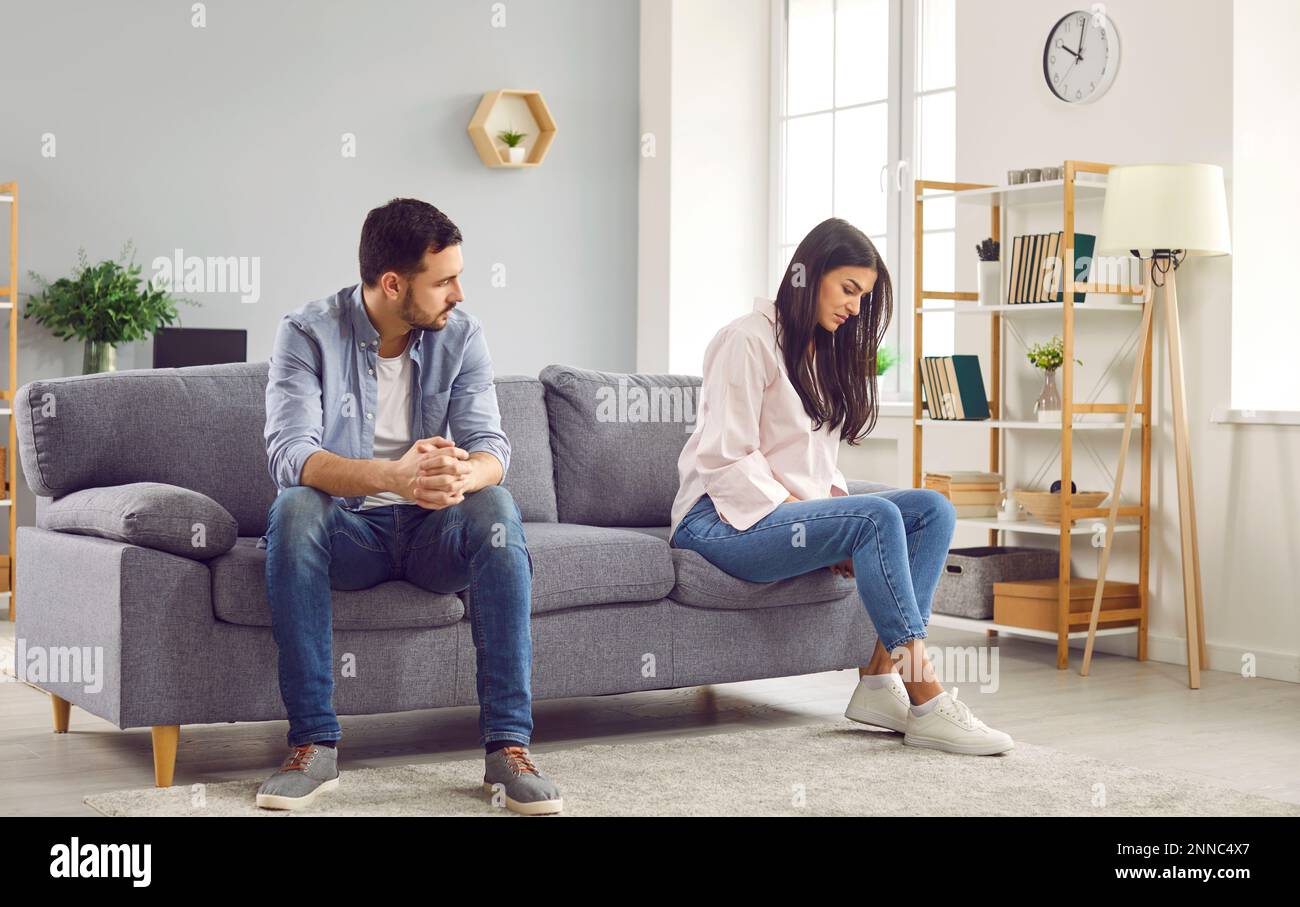 Couple sitting on opposite sides of the sofa at home. Quarrel and divorce concept. Stock Photo